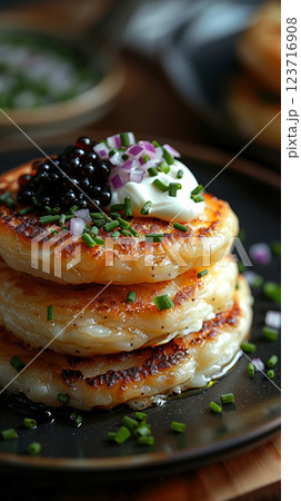 A luxurious plate of golden, fluffy pancakes topped with creme fraiche, caviar, finely chopped red onion, and a sprinkle of green onions. 123716908