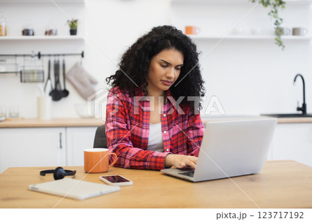 Young African woman sitting at kitchen table using laptop for remote work or study. Casual home environment with focus on technology and productivity. Young African woman sitting at kitchen table using laptop for remote work or study. Casual home environment with focus on technology and productivity. 123717192
