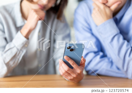 家でスマホを見ながら落ち込むミドル夫婦 123720574