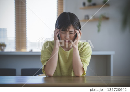 こめかみをおさえてうつむくアラサーの女性 こめかみをおさえてうつむくアラサーの女性 123720642