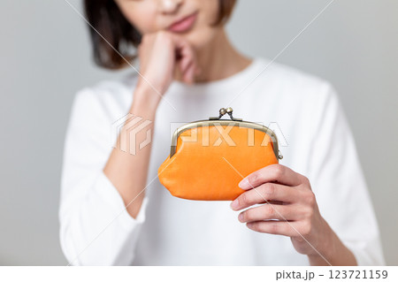 オレンジ色のがま口財布を持って悩むミドル女性 オレンジ色のがま口財布を持って悩むミドル女性 123721159