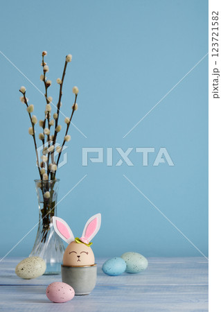 Easter bunny eggs in egg holder on blue background. Multicolored eggs and sprigs of willow. Place for your text 123721582
