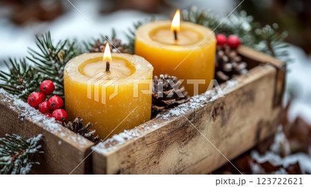 Two lit yellow candles sit in a wooden box decorated with pinecones, branches, and red berries. Concept: cozy winter ambiance. 123722621
