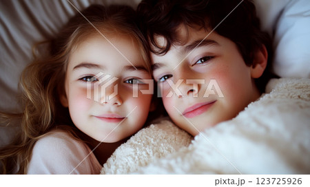 Two children lie closely together, wrapped in a cozy blanket, smiling softly. Concept warmth, comfort, sibling bond. 123725926