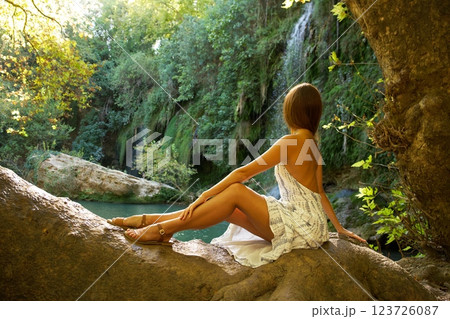Woman Sitting on Tree Trunk Admiring Waterfall View  123726087