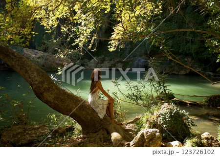 Woman Sitting on Tree Overlooking Waterfall Lagoon  123726102