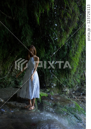 Woman Standing Peacefully Under a Gentle Waterfall Mist  123726113