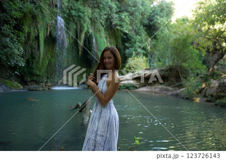 Smiling Woman Standing by a Scenic Waterfall and River  123726143