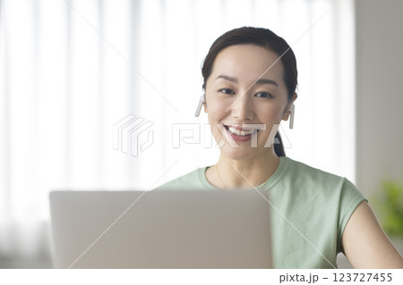 イヤホンをつけてノートパソコンに向かう30代の女性　ビデオチャット　オンライン通話　イメージ 123727455