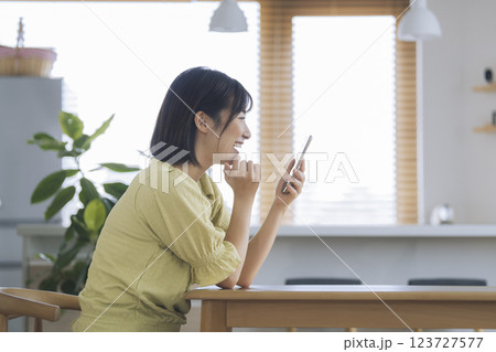 自宅のデーブルでスマホの画面を見る笑顔のアラサーの女性 自宅のデーブルでスマホの画面を見る笑顔のアラサーの女性 123727577