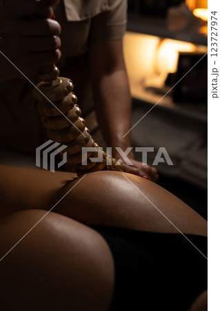 Anti-cellulite massage on the stomach using wooden objects. Massage salon in a dark room. 123727974