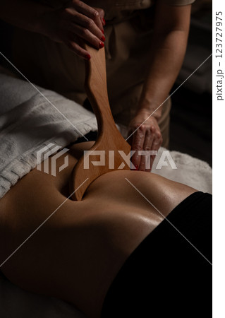 Anti-cellulite massage on the stomach using wooden objects. Massage salon in a dark room. 123727975