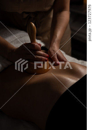 Anti-cellulite massage on the stomach using wooden objects. Massage salon in a dark room. 123727976