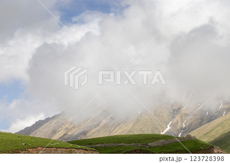 Misty mountains with green hills and rocky slopes partially covered in clouds under a vast blue sky Misty mountains with green hills and rocky slopes partially covered in clouds under a vast blue sky 123728398