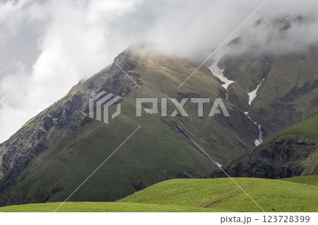 Misty mountain landscape with green slopes, rocky peaks, and a small cascading waterfall in a serene valley. Misty mountain landscape with green slopes, rocky peaks, and a small cascading waterfall in a serene valley. 123728399