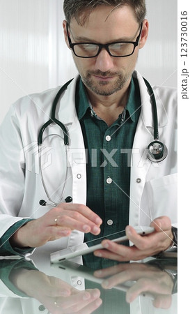 Doctor man in green shirt under a white coat using digital tablet in modern healthcare setting, interacting with patient data, vertical portrait. Medicine concept Doctor man in green shirt under a white coat using digital tablet in modern healthcare setting, interacting with patient data, vertical portrait. Medicine concept 123730016