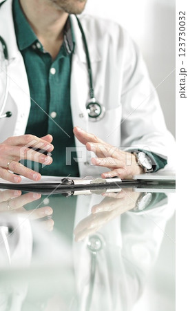 Male doctor using a clipboard and taking notes on glass desk in a medical office, close-up vertical view. Medicine concept Male doctor using a clipboard and taking notes on glass desk in a medical office, close-up vertical view. Medicine concept 123730032