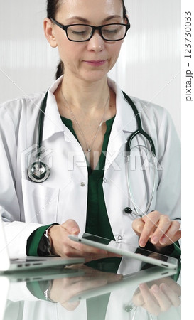 Female doctor in white coat using digital tablet in modern healthcare setting, interacting with patient data, vertical portrait. Medicine concept Female doctor in white coat using digital tablet in modern healthcare setting, interacting with patient data, vertical portrait. Medicine concept 123730033