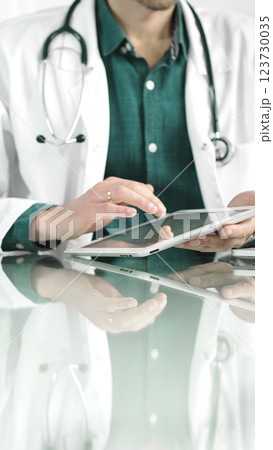 Doctor man in green shirt under a white coat using digital tablet in modern healthcare setting, interacting with patient data. Medicine concept Doctor man in green shirt under a white coat using digital tablet in modern healthcare setting, interacting with patient data. Medicine concept 123730035