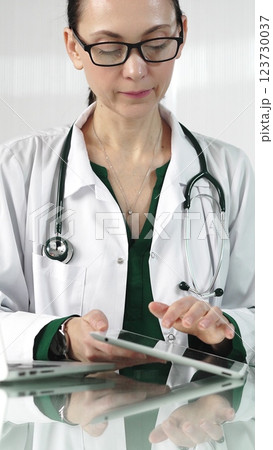 Female doctor in white coat using digital tablet in modern healthcare setting, interacting with patient data, vertical portrait. Medicine concept Female doctor in white coat using digital tablet in modern healthcare setting, interacting with patient data, vertical portrait. Medicine concept 123730037