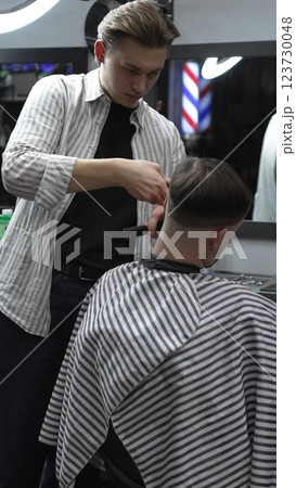 Professional barber carefully trimming customer's hair with electric clipper, providing a stylish and precise haircut in a modern barbershop environment 123730048