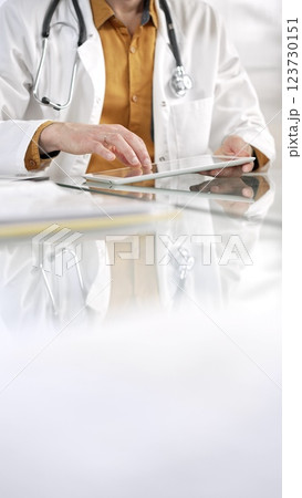 Unknown male doctor wearing a stethoscope, yellow shirt under a lab coat, is using digital tablet in modern healthcare setting, interacting with patient data, vertical portrait. Medicine concept 123730151