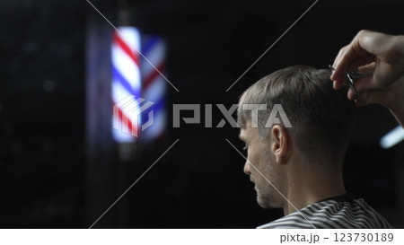 Professional barber grooming male client's hair with scissors, vintage barber pole framing traditional barbershop setting 123730189