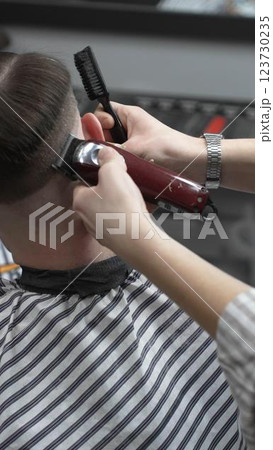 Professional barber grooming client's hair using electric clipper, delivering precise cut with skill in contemporary salon setting, close-up view 123730235