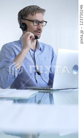 Male office worker demonstrates the significance of technology in modern business through client communication using laptop and headset. Business people concept 123730246
