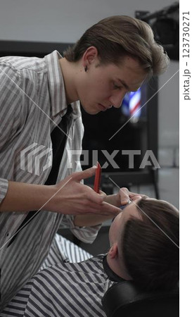 Professional barber trimming customer's hair with electric clipper, focusing on precise nape grooming within contemporary barbershop interior design Professional barber trimming customer's hair with electric clipper, focusing on precise nape grooming within contemporary barbershop interior design 123730271