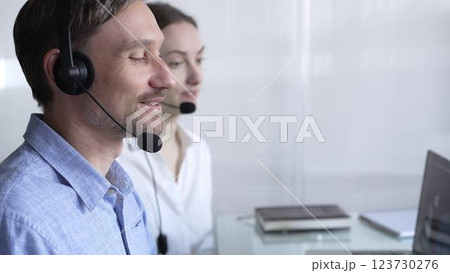 Happy smiling male call center operator in blue casual shirt is assisting clients online, providing customer support and answering inquiries. Business call center 123730276