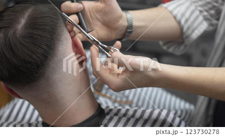 Professional barber cutting client's hair with scissors and comb, creating a stylish fade in a modern barbershop, providing a high quality grooming service 123730278