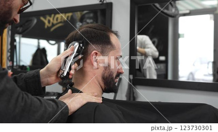 Skilled barber trimming client's hair using electric razor, creating contemporary hairstyle in modern barbershop setting with precise, professional technique Skilled barber trimming client's hair using electric razor, creating contemporary hairstyle in modern barbershop setting with precise, professional technique 123730301
