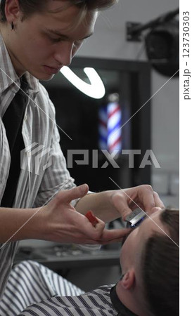 Professional barber trimming customer's hair with electric clipper, focusing on precise nape grooming within contemporary barbershop interior design 123730303