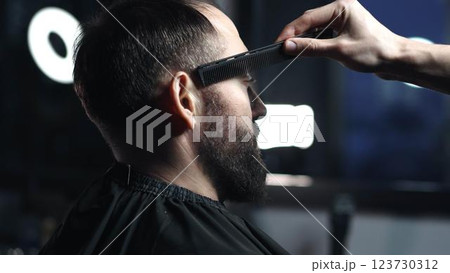 Skilled barber grooming client's hair with precision, working inside contemporary barbershop setting, preparing stylish haircut 123730312