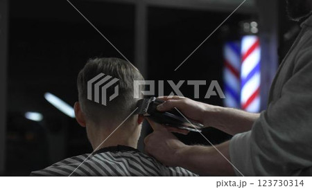 Skilled barber trimming client's hair with electric razor, creating precise contemporary hairstyle inside sleek urban barbershop setting Skilled barber trimming client's hair with electric razor, creating precise contemporary hairstyle inside sleek urban barbershop setting 123730314