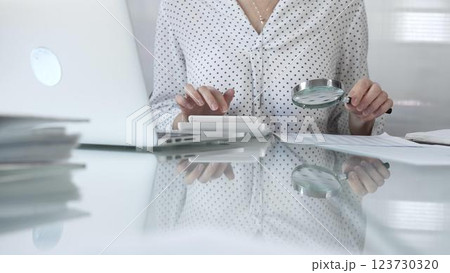 Businesswoman carefully reviewing financial reports with magnifying glass and calculator, conducting audit and analyzing data, closeup view. Taxes and audit in business 123730320