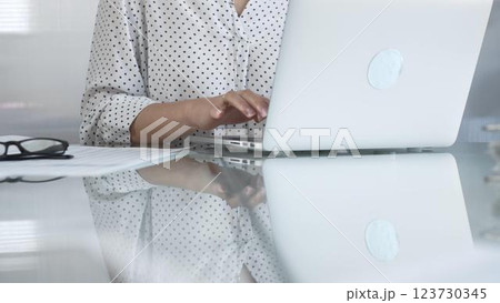 Businesswoman typing on laptop keyboard, preparing taxes and audit reports, with documents and eyeglasses on glass desk. Taxes, audit in business 123730345