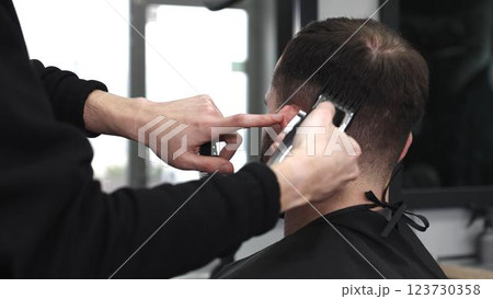 Professional barber trimming male client's hair with electric razor, delivering precise grooming service in contemporary, well lit barbershop setting Professional barber trimming male client's hair with electric razor, delivering precise grooming service in contemporary, well lit barbershop setting 123730358