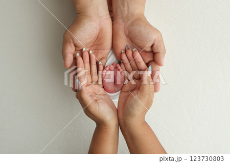 A father and mother hold the feet of a newborn child in a white blanket on a white background.. The feet of a newborn in the hands of parents. Photo of foot, heels and toes.The palms of the parents. 123730803