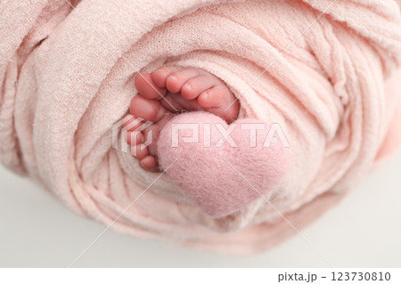 Soft feet of a new born in a wool pink blanket. Closeup of toes, heels and feet of a newborn. Knitted pink heart in the legs of baby. Macro studio photography The tiny foot of a newborn baby.  123730810