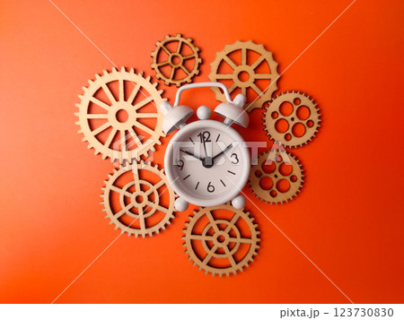 Top view white alarm clock with wooden gear on a orange background. 123730830