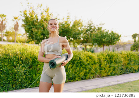 A Cheerful Young Woman Practicing Yoga with a Yoga Mat in a Beautiful Outdoor Setting A Cheerful Young Woman Practicing Yoga with a Yoga Mat in a Beautiful Outdoor Setting 123730895