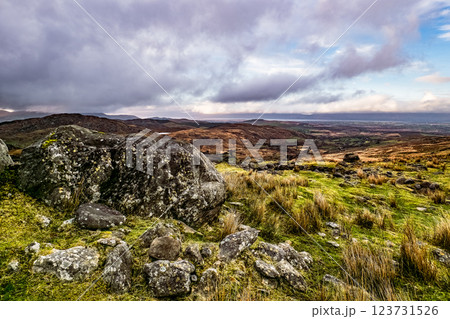 A large rock sits in the foreground, surrounded by grass and scattered stones. In the distance, rolling hills stretch out under a clear sky, showing the beauty of nature. 123731526