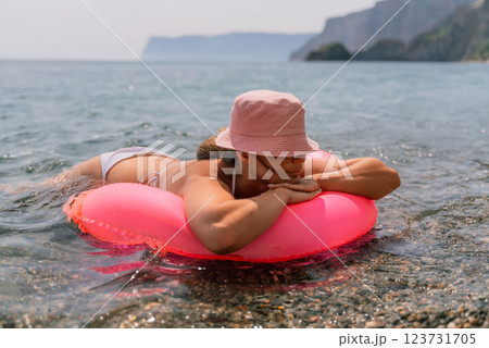 A woman is laying on a pink inflatable raft in the ocean. The scene is peaceful and relaxing, with the woman enjoying the water and the sun. A woman is laying on a pink inflatable raft in the ocean. The scene is peaceful and relaxing, with the woman enjoying the water and the sun. 123731705