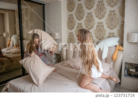 Pillow Fight Bedroom Girls Fun: Two blonde girls playfully fight pillows on a bed in a modern bedroom, enjoying leisure time. Pillow Fight Bedroom Girls Fun: Two blonde girls playfully fight pillows on a bed in a modern bedroom, enjoying leisure time. 123731719