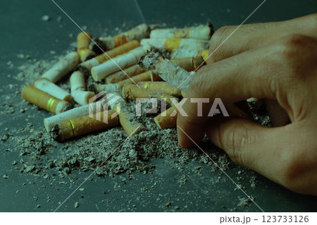 hands holding cigarettes and messy cigarette butts on green gray background hands holding cigarettes and messy cigarette butts on green gray background 123733126