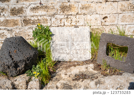 Old stone inscription with Arabic script resting against weathered wall in Northern Cyprus. Ancient artifact, surrounded by grass and volcanic stones, reflects the region historical and cultural depth Old stone inscription with Arabic script resting against weathered wall in Northern Cyprus. Ancient artifact, surrounded by grass and volcanic stones, reflects the region historical and cultural depth 123733283