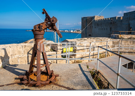 Old artillery mechanism on the fortress walls of Kyrenia in Northern Cyprus. The aged military relic stands against the backdrop of the sea and historic castle, symbolizing the island turbulent past Old artillery mechanism on the fortress walls of Kyrenia in Northern Cyprus. The aged military relic stands against the backdrop of the sea and historic castle, symbolizing the island turbulent past 123733314