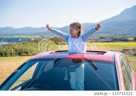 Little girl joyfully sticks out of car sunroof with raised hands against the backdrop of mountains in Northern Cyprus. The image symbolizes freedom, adventure, and the excitement of travel with child 123733325